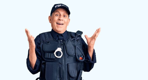Älterer, gutaussehender Mann in Polizeiuniform feiert den Sieg mit glücklichem Lächeln und Siegerausdruck mit erhobenen Händen  - Foto, Bild