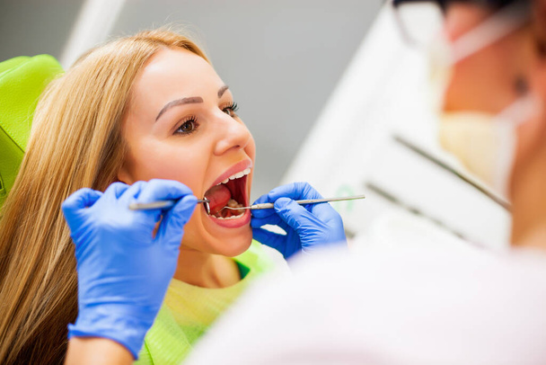 Junge Frau beim Zahnarzt. Zahnarzt untersucht ihre Zähne. - Foto, Bild