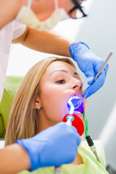 Mujer joven en el dentista. El dentista está reparando sus dientes.. - Foto, imagen