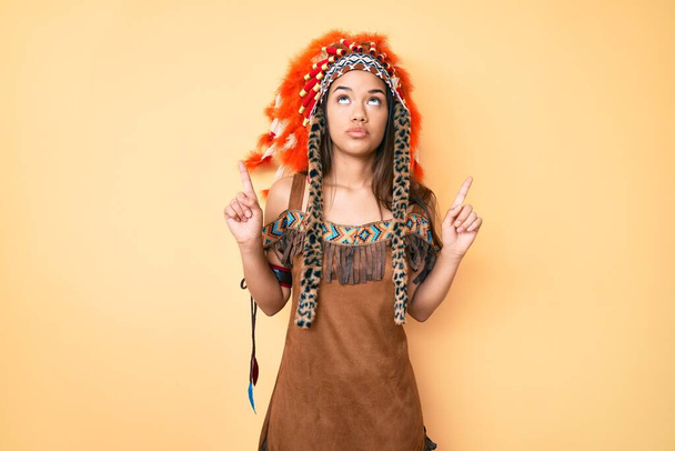 Młoda piękna Latynoska ubrana w indiański kostium, wyglądająca smutno i smutno, wskazująca kierunek palcami, nieszczęśliwa i przygnębiona.  - Zdjęcie, obraz