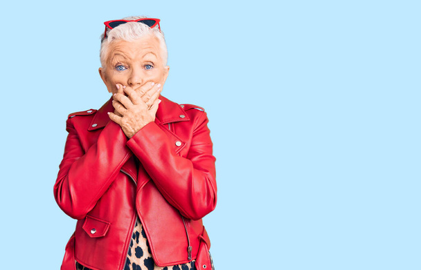 Senior beautiful woman with blue eyes and grey hair wearing a modern style with a red leather jacket shocked covering mouth with hands for mistake. secret concept.  - Photo, Image