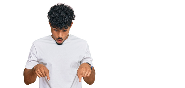 Молодий арабський чоловік в повсякденній білій сорочці вказує вниз пальцями, показуючи рекламу, здивоване обличчя і відкритий рот
  - Фото, зображення