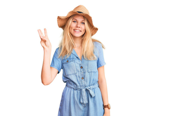 Young beautiful blonde woman wearing summer hat and dress showing and pointing up with fingers number three while smiling confident and happy.  - Valokuva, kuva
