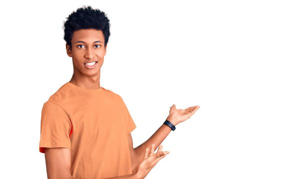 Young african american man wearing casual clothes inviting to enter smiling natural with open hand  - Foto, Imagem