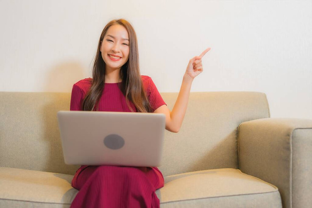 Портрет красивая молодая азиатская женщина использовать ноутбук на диване в интерьере гостиной - Фото, изображение