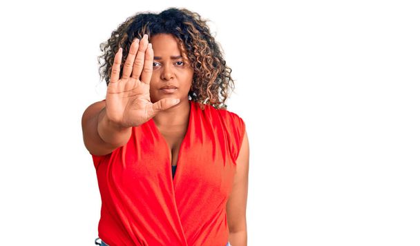 Młoda Afroamerykanka plus size kobieta w luźnym stylu z koszulą bez rękawów robi stop śpiewać z dłoni. wyraz ostrzegawczy z negatywnym i poważnym gestem na twarzy.  - Zdjęcie, obraz