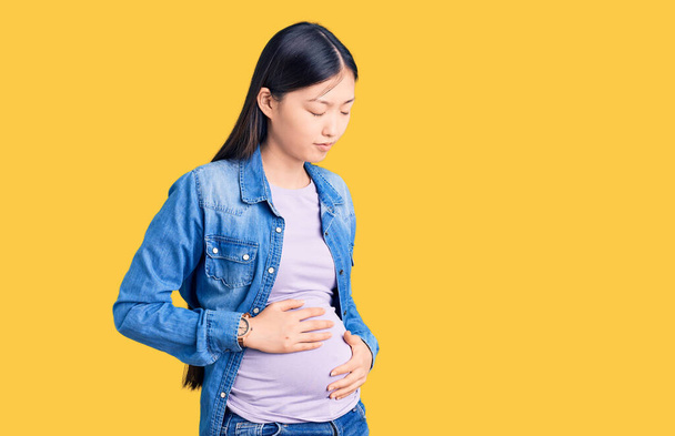 消化不良、痛みを伴う病気が体調不良のため、若い美しい中国の女性は胃の上に手で赤ちゃんを期待。キャッシュ・コンセプト.  - 写真・画像
