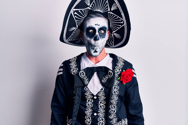 Молодой человек, одетый в мексиканский день мертвого костюма поверх белого, делает рыбье лицо с губами, сумасшедший и смешной жест. Смешное выражение.  - Фото, изображение