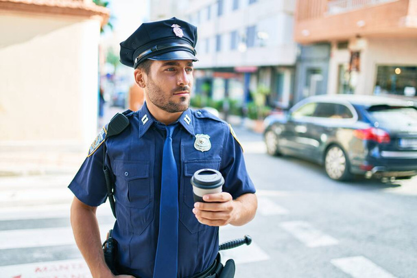 Junge hispanische Polizisten in Polizeiuniform mit ernstem Gesichtsausdruck. Kaffeetasse zum Mitnehmen steht an der Stadtstraße. - Foto, Bild
