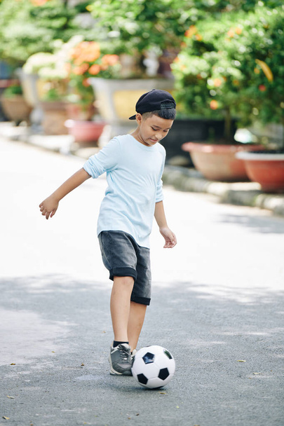 Kind spielt Fußball allein auf der Straße und lernt, wie man den Ball hüpft - Foto, Bild