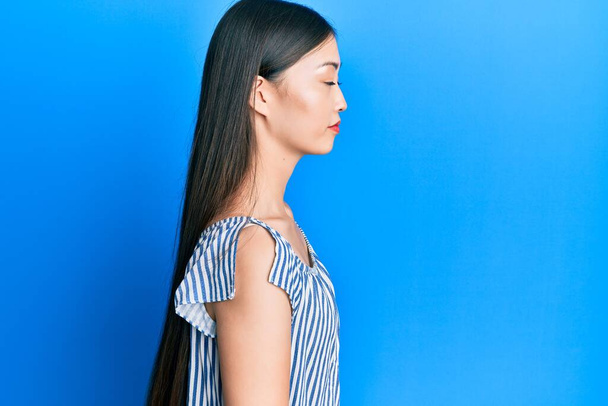 Jeune femme chinoise portant un t-shirt rayé décontracté regardant vers le côté, pose de profil relax avec un visage naturel avec un sourire confiant.  - Photo, image