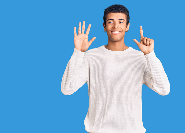 自信を持って幸せな笑みを浮かべている間、若いアフリカ系アメリカ人の男性は、カジュアルな服を着て指の数7を示すと指摘.  - 写真・画像