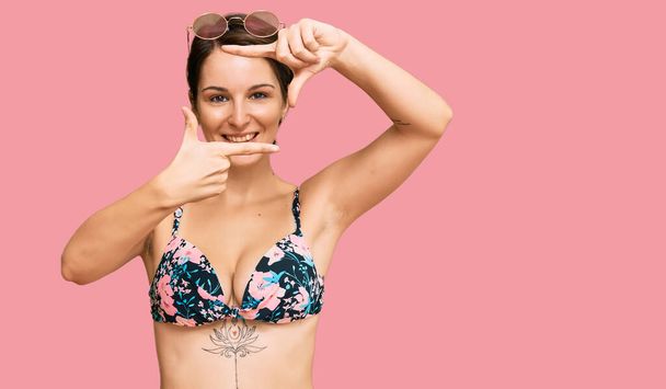 Young brunette woman with short hair wearing bikini smiling making frame with hands and fingers with happy face. creativity and photography concept.  - Photo, Image