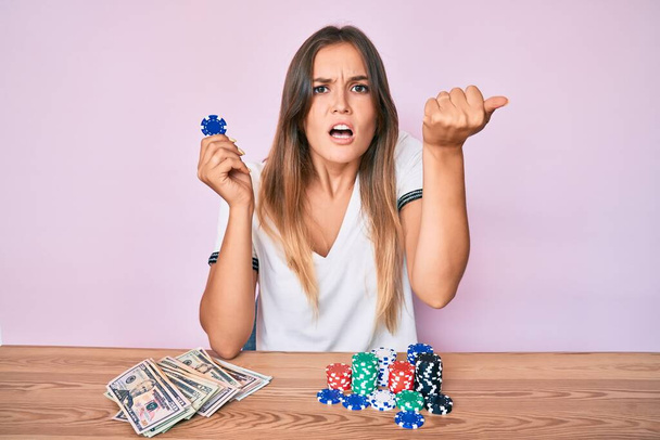 Beautiful caucasian woman playing poker holding casino chips annoyed and frustrated shouting with anger, yelling crazy with anger and hand raised  - Photo, Image