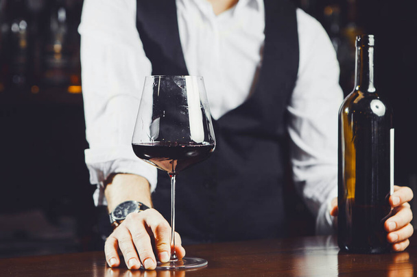 Bartender at the bar with a glass of red wine and bottle, close-up. - 写真・画像