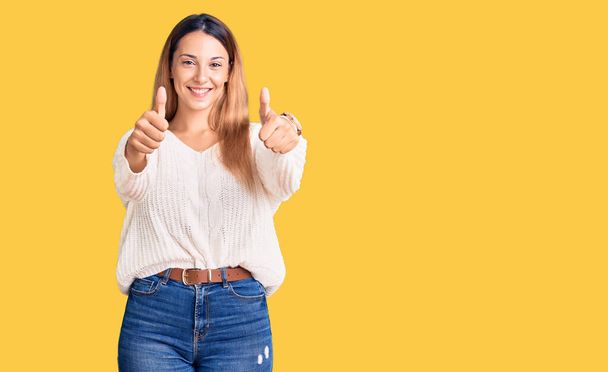 Beautiful young woman wearing casual clothes approving doing positive gesture with hand, thumbs up smiling and happy for success. winner gesture.  - Photo, Image
