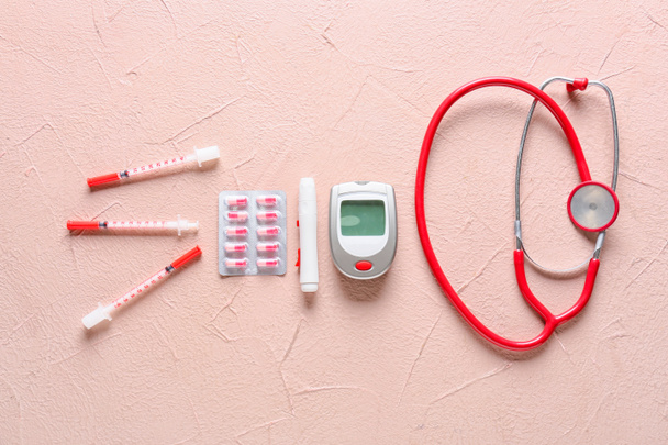 Blutzuckermessgerät mit Lanzettstift, Pillen, Spritzen und Stethoskop auf farbigem Hintergrund. Diabetes-Konzept - Foto, Bild
