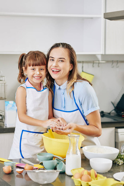 Porträt einer glücklich umarmten jungen Mutter und ihrer Tochter mit Mehl auf der Nase beim gemeinsamen Kochen - Foto, Bild