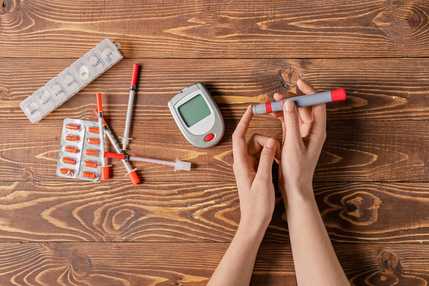Female hands with lancet pen, glucometer, pills and syringes on wooden background. Diabetes concept - Zdjęcie, obraz