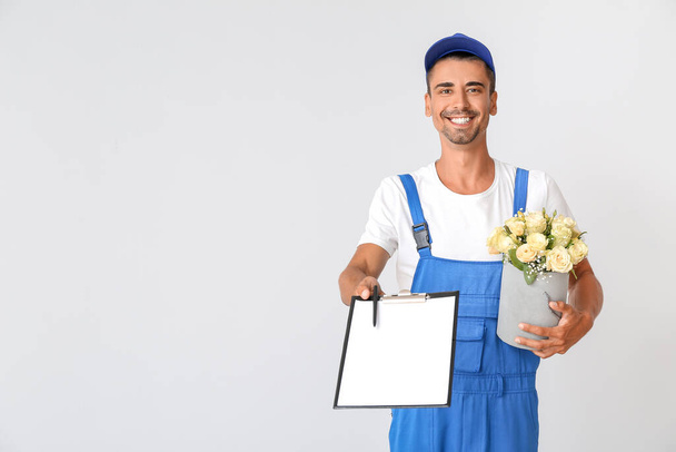 Delivery man with bouquet of flowers and clipboard on light background - Photo, Image