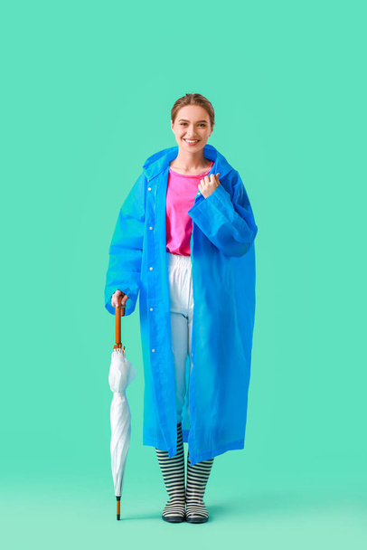 Beautiful young woman in raincoat and with umbrella on color background - Foto, afbeelding