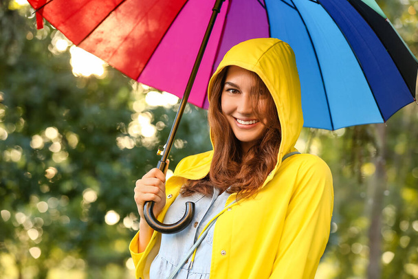 Beautiful young woman with umbrella wearing raincoat in park - Photo, Image