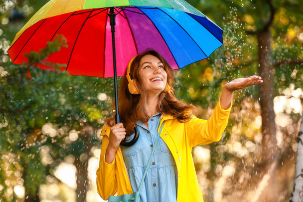 Mooie jonge vrouw met paraplu in regenjas in park - Foto, afbeelding