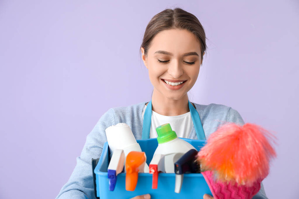 Young woman with cleaning supplies on color background - Foto, afbeelding