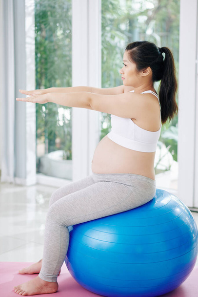 Terhes ázsiai nő gyakorolja a fitness labda otthon reggel - Fotó, kép