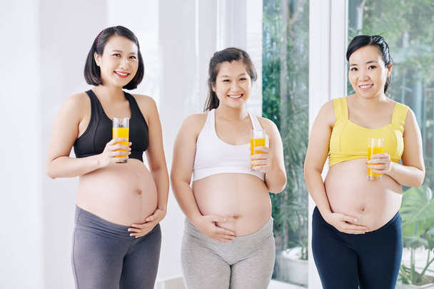 Groupe de femmes vietnamiennes gaies enceintes debout avec des verres de jus frais - Photo, image