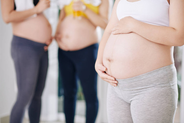 Cropped image of pregnant woman in crop top and soft leggings touching her big belly - Photo, Image