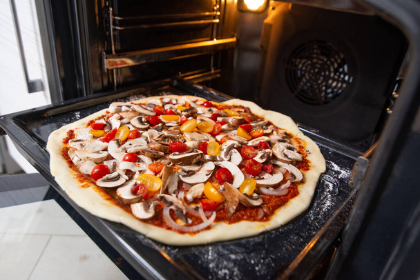 The raw pizza on a baking sheet in the oven. Vegan food. - 写真・画像