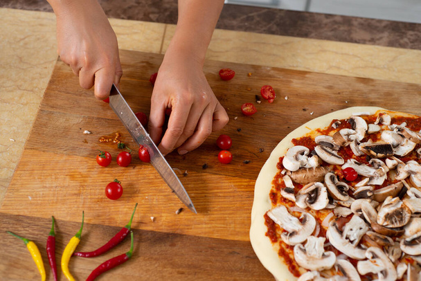 Widok z góry ręce szefa kuchni siekanie z nożem pomidory wiśniowe na drewnianej desce. Gotowanie pizzy wegańskiej. - Zdjęcie, obraz