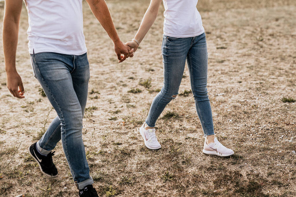 Nahaufnahme eines romantischen Paares, das sich an den Händen hält und auf Sand spaziert. Fokus auf die Füße und Hände der Familie - Foto, Bild