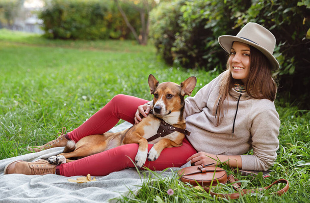Smiling woman in hat with and her dog sitting on plaid in an autumn park. - Foto, imagen