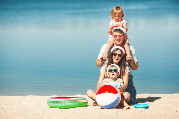 Concetto natalizio. Famiglia che indossa berretti di Natale in spiaggia - Foto, immagini