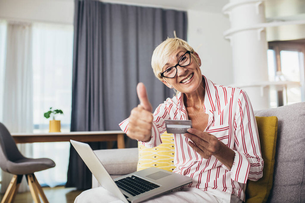 Usmívající se starší žena nakupování on-line s kreditní kartou pomocí notebooku. - Fotografie, Obrázek