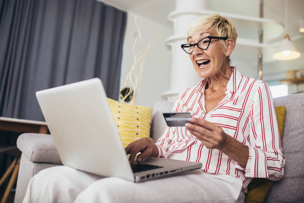 Sonriendo mujer madura de compras en línea con tarjeta de crédito utilizando el ordenador portátil. - Foto, Imagen
