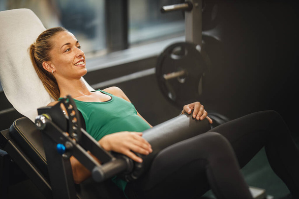 Spor giyim bölümünde spor salonunda çalışan kaslı genç bir kadının fotoğrafı. Kalça güven makinesinde kalça köprüsü egzersizi yapıyor.. - Fotoğraf, Görsel
