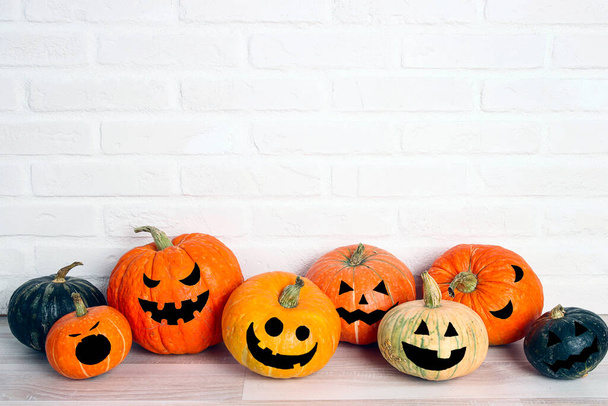 Halloween pumpkin head Jack lantern with funny faces on the table against a white brick wall background. Copy space for text. - Fotó, kép