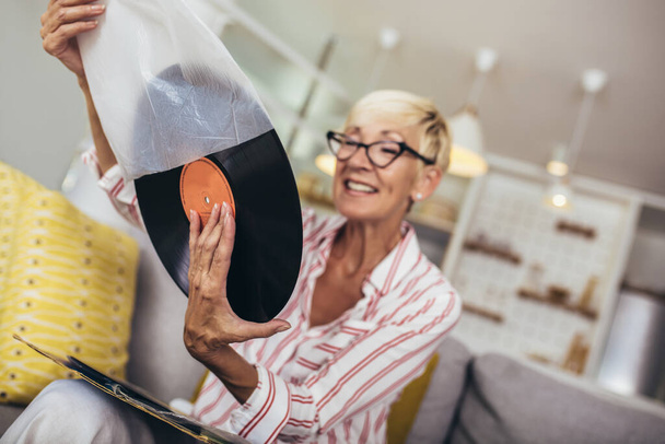Happy senior woman listening vinyl at home. Choosing next record. - Photo, Image
