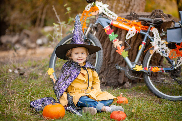 Ein kleines Mädchen im Halloween-Urlaub in der Natur, ein Kind in der Nähe eines Fahrrads  - Foto, Bild