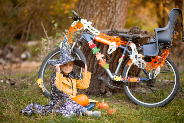 Dívka na Halloween dovolená v přírodě, dítě sedí v blízkosti kola zdobené girlandy - Fotografie, Obrázek