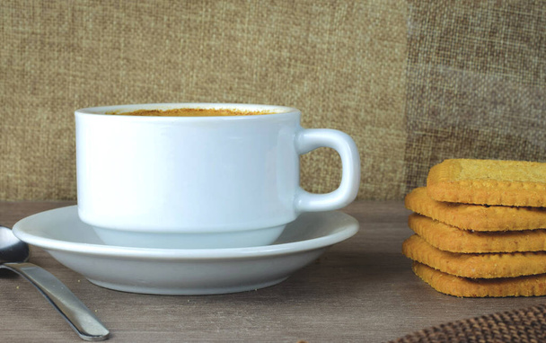 Πρωινό πρωί-πρωί, λευκό πορσελάνινο φλιτζάνι με καφέ με γάλα, συνοδευόμενο από ψημένα μπισκότα - Φωτογραφία, εικόνα