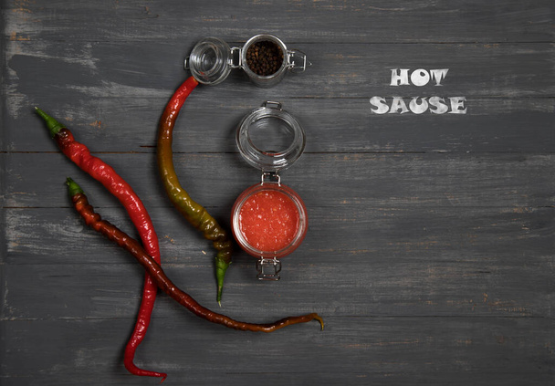 Sauce in a glass jar of red hot pepper on a dark background with pods and chalk lettering. Horizontal orientation - Photo, Image