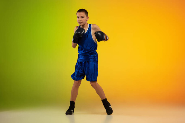 Teenage boxer against gradient neon studio background in motion of kicking, boxing - Foto, afbeelding