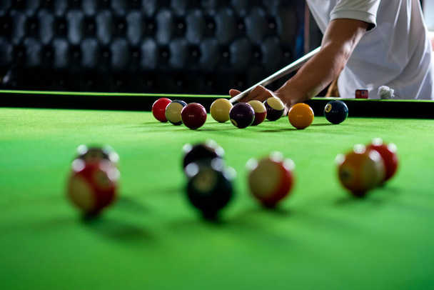 Man's hand and Cue arm playing snooker game or preparing aiming to shoot pool balls on a green billiard table. Colorful snooker balls on green frieze - Фото, изображение