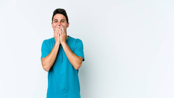 Νεαρός καυκάσιος άνδρας απομονωμένος σε λευκό φόντο γελώντας για κάτι, καλύπτοντας το στόμα με τα χέρια. - Φωτογραφία, εικόνα