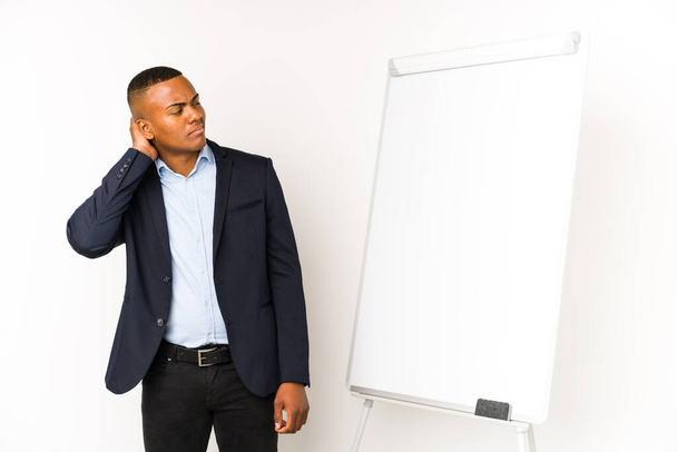 Young latin man with a white board isolated on a white background touching back of head, thinking and making a choice. - Photo, Image