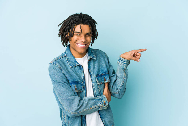 Young black man wearing a jeans jacket smiling cheerfully pointing with forefinger away. - 写真・画像